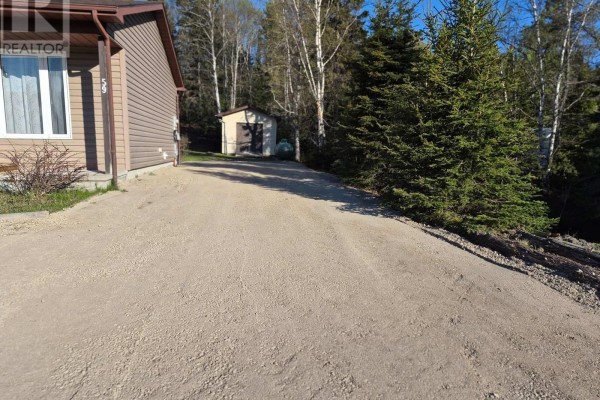 Gravel driveway extending past the house towards a small shed and wooded area in the background. - 59 Hemlo Drive, Marathon