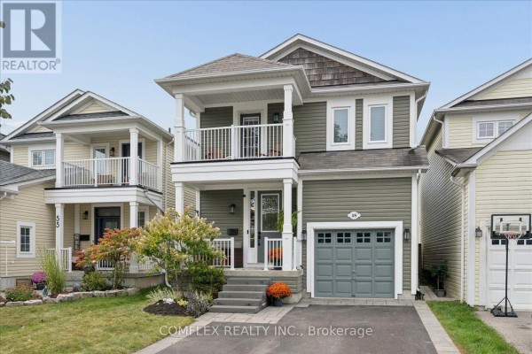 Front exterior of a two-story green house with a grey garage door and covered porch. - 59 Hodnett Crescent, Clarington