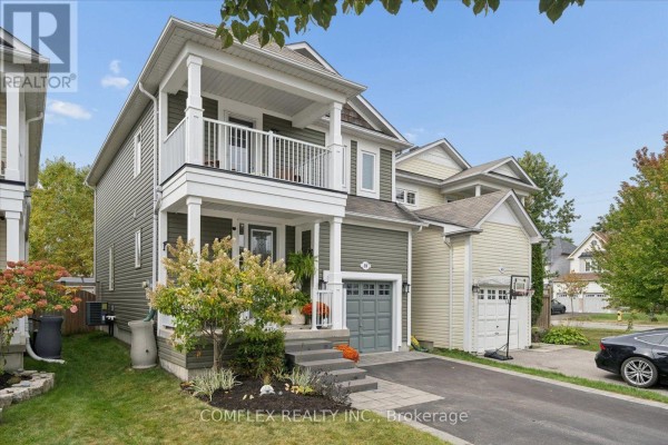 Side view of a two-story green house with a grey garage door and driveway. - 59 Hodnett Crescent, Clarington