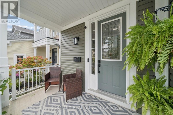 Covered front porch with two chairs, a rug, and a hanging fern beside the grey front door. - 59 Hodnett Crescent, Clarington