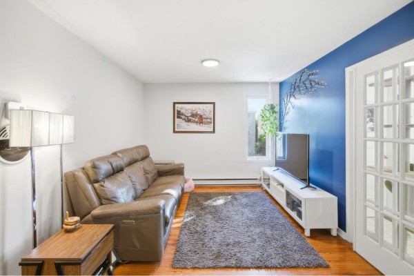 Living room with a brown leather sofa, gray rug, and a TV on a white stand. - 59 Rue Des Carouges, #3, Gatineau