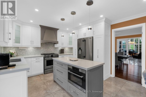 Modern kitchen with white cabinets, grey island, stainless steel appliances, and a view into a dining area. - 590 Gagnon Place, Newmarket