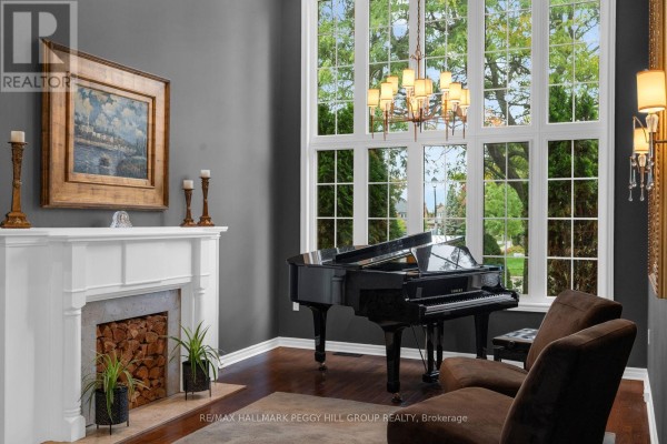 Living room with a grand piano, white fireplace with wood storage, and large windows. - 590 Gagnon Place, Newmarket