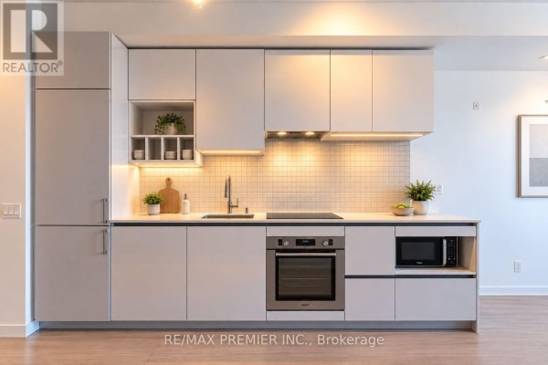 Close-up of a sleek white kitchen with integrated appliances, tiled backsplash, and under-cabinet lighting. - 5901 - 950 Portage Parkway, Vaughan