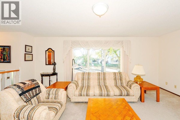 Living room with beige carpet, sofa, armchair, coffee table, and a large window. - 5907 43 Avenue, Camrose