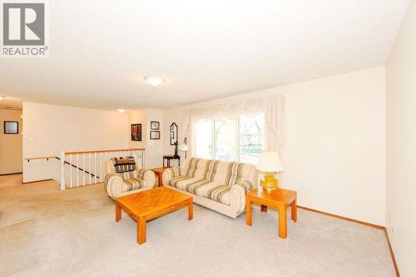 Living room with beige carpet, sofa, armchair, coffee table, and view of staircase. - 5907 43 Avenue, Camrose