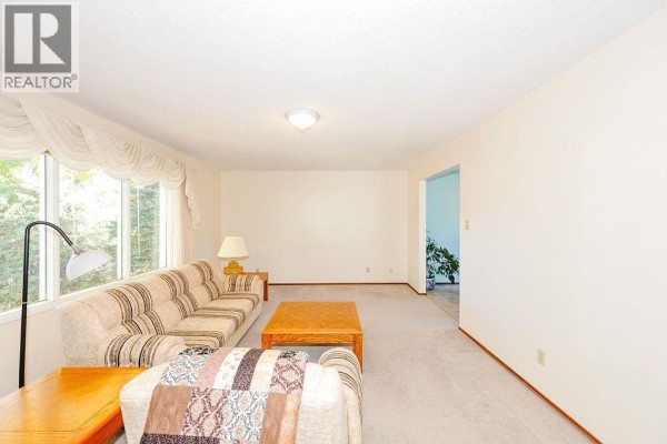 Living room with beige carpet, sofa, coffee table, and doorway to another room. - 5907 43 Avenue, Camrose