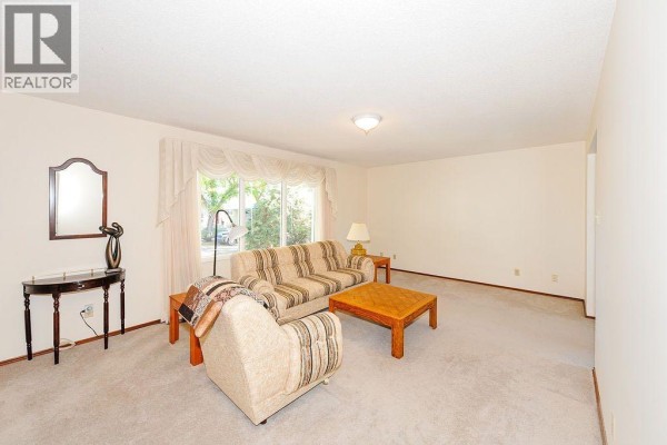 Living room with beige carpet, sofa, armchair, coffee table, and a decorative mirror. - 5907 43 Avenue, Camrose