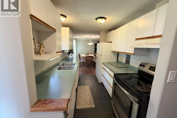 Outbuilding with vehicles parked outside, featuring a gravel area and trees nearby. - 591 Davidson Crescent, Lillooet