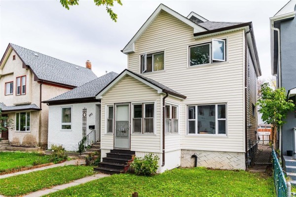 Side view of the light beige vinyl-sided two-story house showing the front porch and windows. - 591 Home Street, Winnipeg