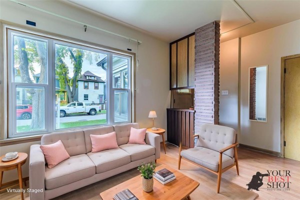 Living room with a beige sofa, accent chairs, coffee table, and large bay window. - 591 Home Street, Winnipeg