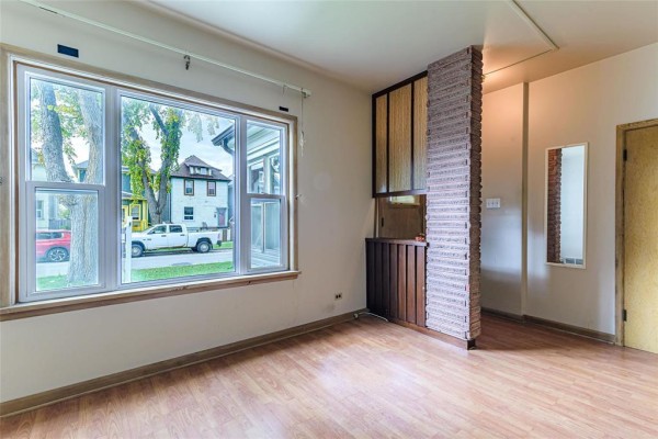 Living room with light wood floors, a decorative brick partition, and a large window. - 591 Home Street, Winnipeg