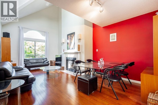 Living room with vaulted ceiling, fireplace, black leather sofas, glass coffee table, and dining area. - 592 W 16th Avenue, Vancouver