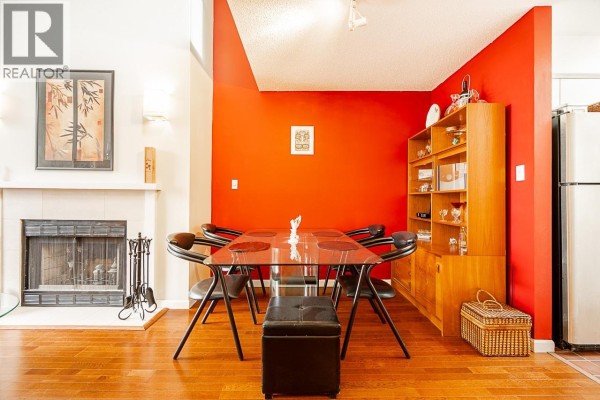 Dining area with glass table, black chairs, wood cabinet, red accent wall, and fireplace with hearth. - 592 W 16th Avenue, Vancouver