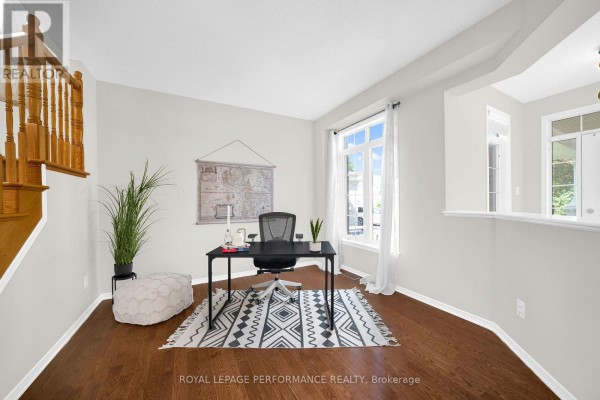 Home office with a desk, chair, large window, hardwood floors, and wooden staircase. - 593 Pinawa Circle, Ottawa