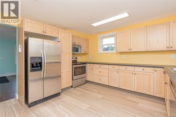 Kitchen with light wood cabinets, stainless steel refrigerator and oven, and yellow walls. - 5934 Highland Ave, Duncan
