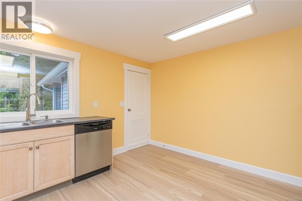 Kitchen sink, dishwasher, and doorway with light wood cabinets and bright yellow walls. - 5934 Highland Ave, Duncan
