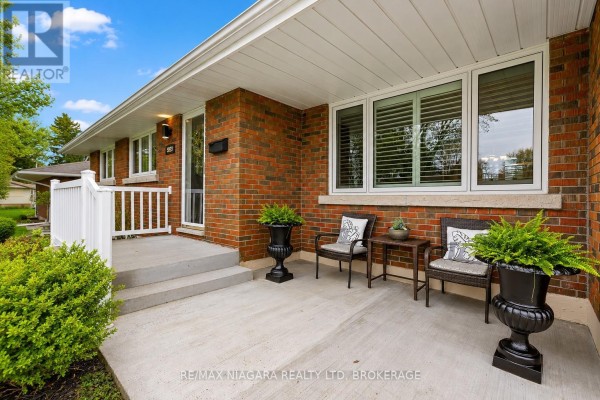 Front porch of the bungalow with two chairs, a small table, and potted plants. - 5938 Stevens Street, Niagara Falls