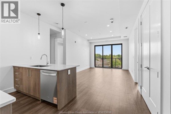Open-concept living area and kitchen with a large sliding glass door and a central island. - 595 Lily Mac Unit# 205, Windsor