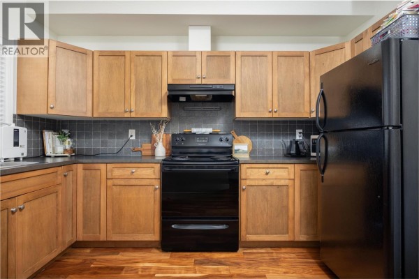 View of a kitchen area with light wood cabinets, dark grey countertops, and black appliances. - 5951 Heritage Drive Unit# 10, Vernon