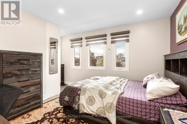 Bedroom with wooden dresser, patterned bedding, and three windows - 5952 Grossbeak Drive Mississauga