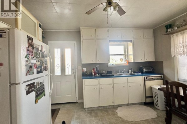 Kitchen with white cabinets, blue countertops, and a white refrigerator covered in photos. - 5952 Okanagan Street, Oliver