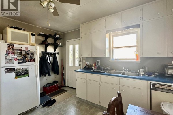 Kitchen interior with a white refrigerator, entryway door, and white cabinets with blue countertops. - 5952 Okanagan Street, Oliver