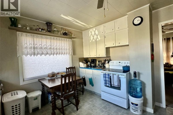 Kitchen with white cabinets, blue countertops, a stove, a small dining table, and a window. - 5952 Okanagan Street, Oliver