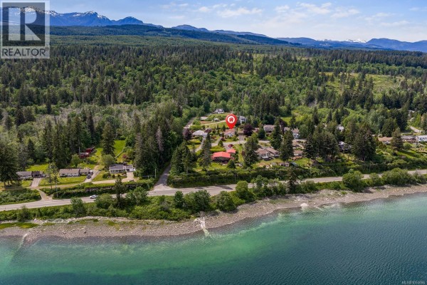 Aerial view of residential homes along a waterfront road with a forest and mountains in background. - 5989 Garvin Rd, Union Bay