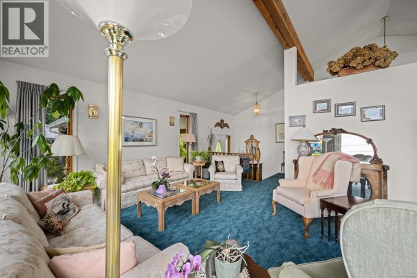 Living room with floral sofas, blue carpet, exposed beams, and decorative mirror on the wall. - 5989 Garvin Rd, Union Bay