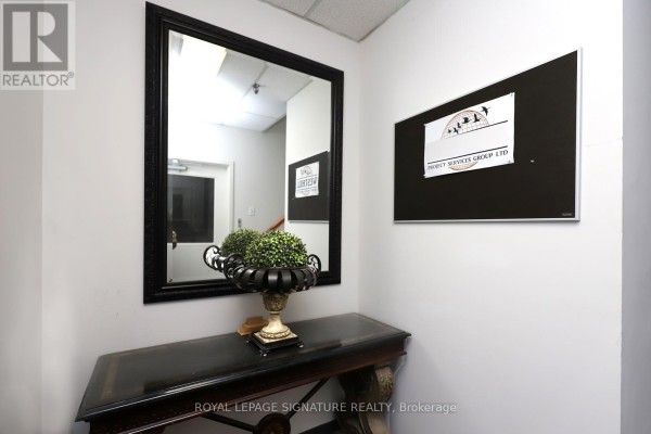 Hallway entrance with a large decorative mirror, console table with plant, and framed company sign. - 5a - 2740 Matheson Boulevard, Mississauga
