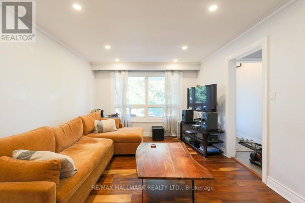 Living room with a large orange sectional sofa, wooden coffee table, and television. - 5a Scotia Avenue, Toronto