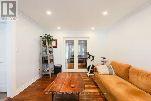 Living area with an orange sofa, exercise equipment, and glass-paned double doors. - 5a Scotia Avenue, Toronto