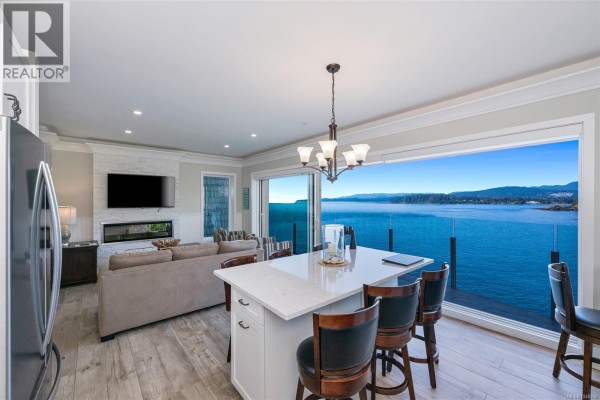 Living room with a fireplace, sofa, and island with bar stools facing the ocean view. - 5b 1000 Sookepoint Pl, Sooke