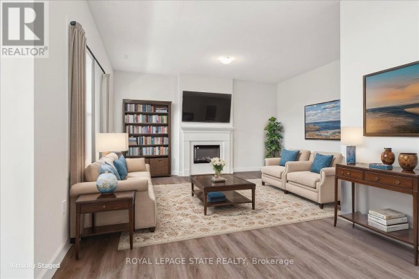 Living room with a fireplace, mounted television, two sofas, a coffee table, and a bookshelf. - 5b Shores Lane, Fort Erie