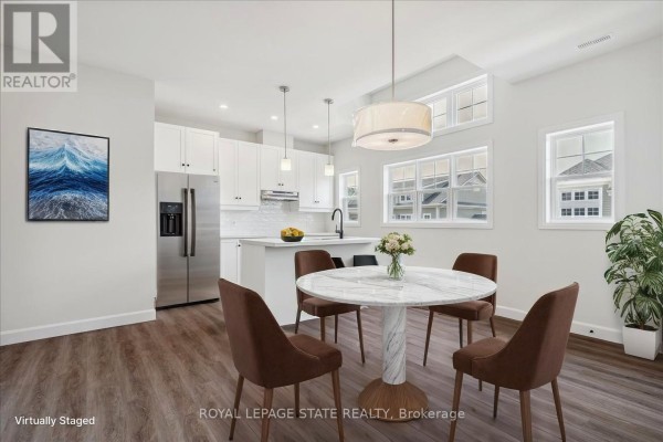 Dining area with a round marble table and chairs adjacent to a white kitchen with stainless steel appliances. - 5b Shores Lane, Fort Erie