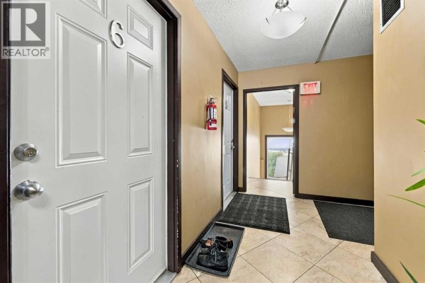 Hallway view showing apartment doors, floor mats, and an exit sign. - 6, 1905 11 Avenue Sw, Calgary