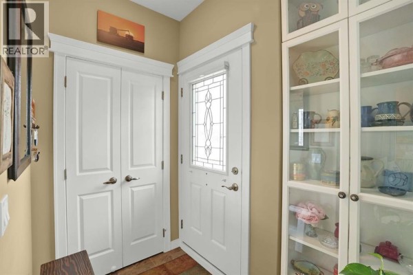 Interior hallway with a glass-paned front door, double white doors, and a white display cabinet. - 6, 20 River Heights View, Cochrane