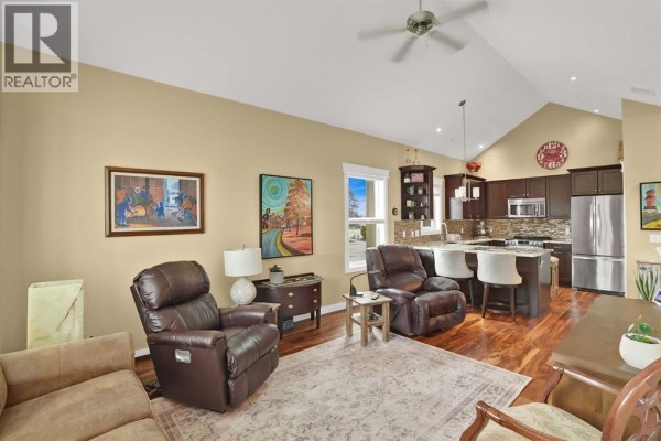 Living room and kitchen area with vaulted ceiling, dark leather recliners, and stainless steel appliances. - 6, 20 River Heights View, Cochrane