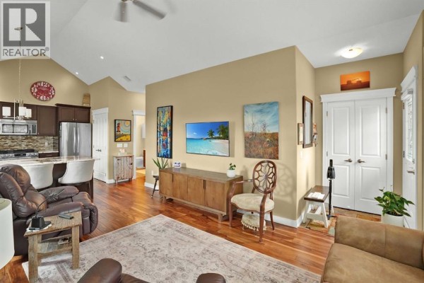 Living area showing recliners, TV, kitchen, and hallway doors with hardwood floors throughout. - 6, 20 River Heights View, Cochrane