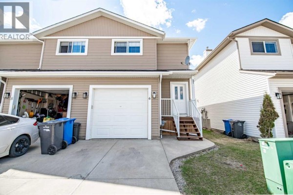 Backyard view of a townhouse complex with green grass and chain-link fencing. - 6, 2002 22 Avenue, Bowden