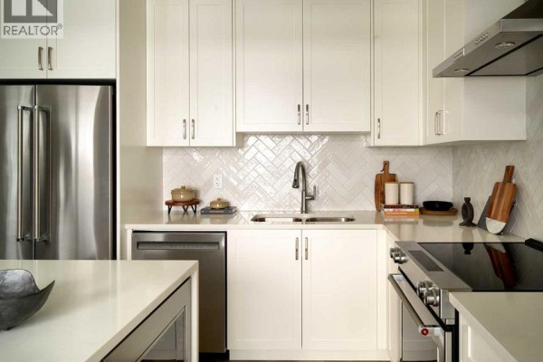Close-up view of a kitchen sink and dishwasher area with white tile backsplash and light wood cabinets. - 6, 20830 Main Street Se, Calgary