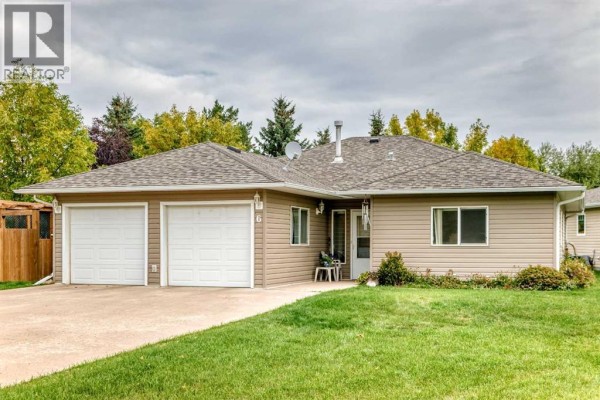 Front exterior of a beige bungalow with a large lawn and mature trees. - 6, 6500 40 Avenue, Stettler