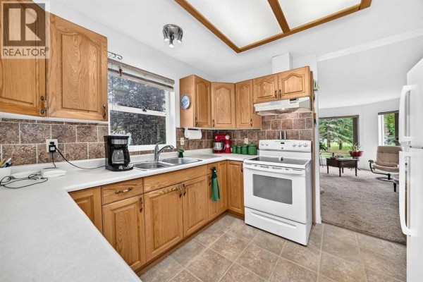 Kitchen with light oak cabinets, beige tiled backsplash, and white appliances. - 6, 6500 40 Avenue, Stettler