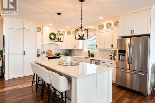 L-shaped white kitchen with a large island, pendant lights, and a stainless steel refrigerator. - 6, 715034 Range Road 73, Rural Grande Prairie No  1, County Of