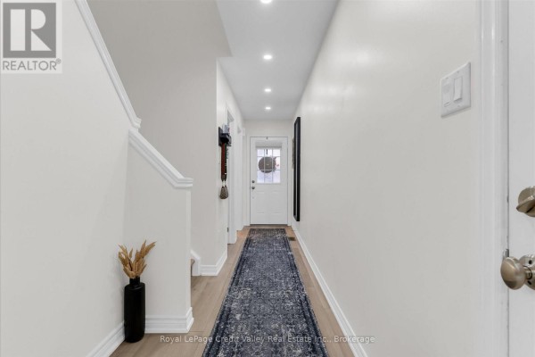 Hallway with white walls, wood floors, a runner rug, and a front door view. - 6 - 10 Pumpkin Pass, Hamilton