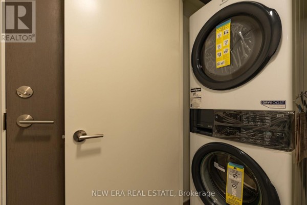 Stacked white washer and dryer unit next to a closed grey door with brushed nickel hardware. - 506 - 10 Wilby Crescent, Toronto