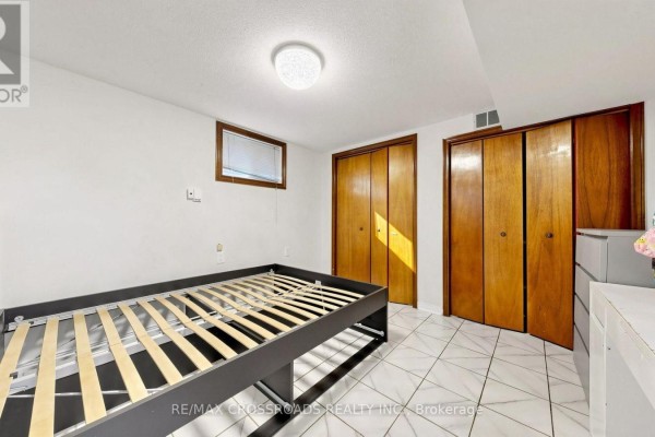 Bedroom with a slatted bed frame, tiled floor, and wooden double closet doors. - 6 - 106 Stilecroft Drive, Toronto