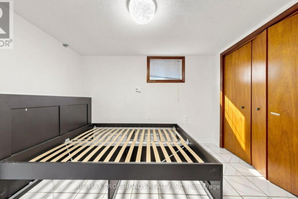 Bedroom with a slatted bed frame, tiled floor, and wooden double closet doors. - 6 - 106 Stilecroft Drive, Toronto