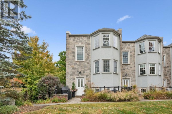 Exterior of a stone townhouse with bay windows, white doors, and a patio with chairs. - 6 - 12 Glasgow Street S, Guelph